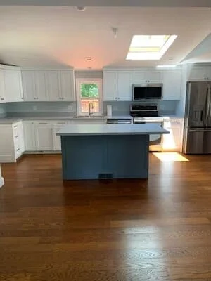 Medium-tone hardwood flooring in kitchen with white cabinets and blue island