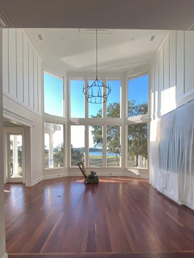 Medium-dark hardwood flooring installed in bay window room with white walls and water views