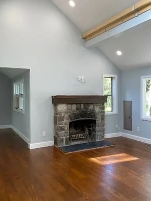 Medium-tone hardwood flooring installed in living room with stone fireplace and exposed beam ceiling