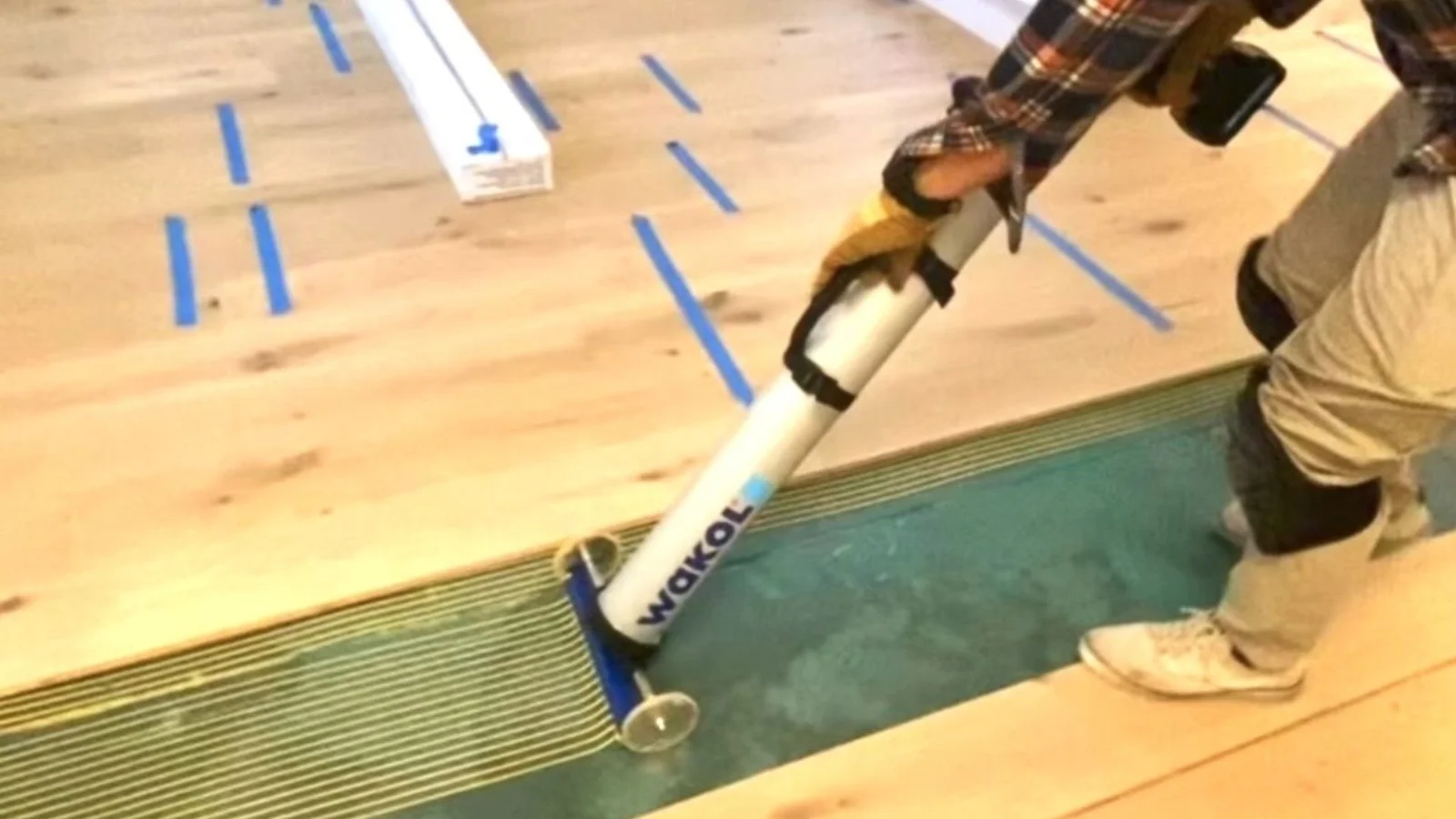 Hardwood floor installation with pneumatic nailer, blue tape layout guides, and light wood planks
