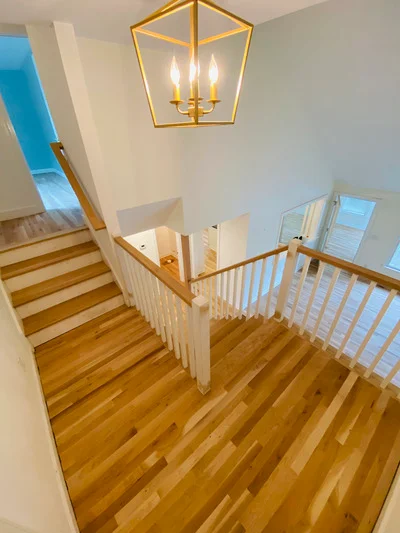 Solid hardwood flooring on staircase and landing with white railings and brass light fixture