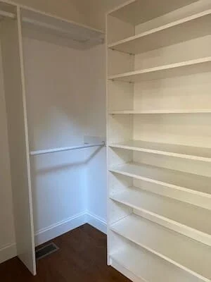 Dark hardwood flooring in walk-in closet with white shelving and rod