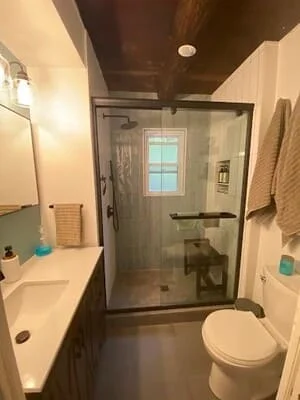 Dark hardwood flooring in bathroom with white vanity, toilet, and frameless glass shower enclosure