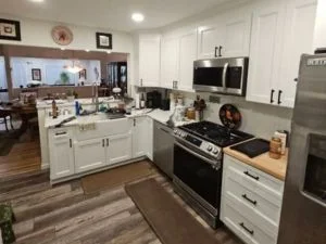 Warm-toned hardwood flooring installed in kitchen with white cabinetry and stainless steel appliances