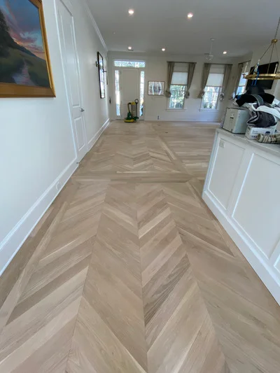 Herringbone pattern hardwood flooring in neutral tones with white trim and recessed lighting