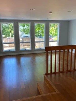 Dark hardwood flooring installed in open room with four glass doors and wood stair railing